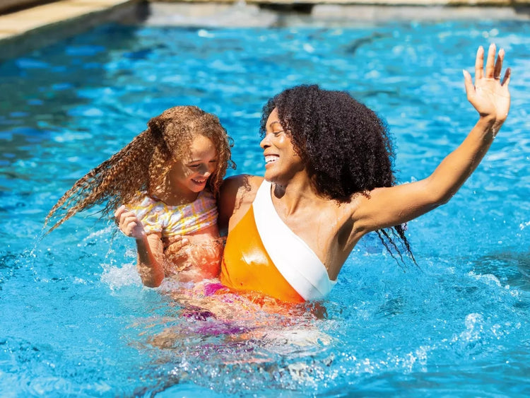 A mother and her daughter laughing and playing together in a clear blue swimming pool.