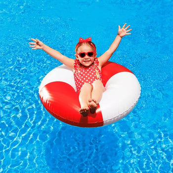 A happy young girl wearing red polka-dot swimwear and heart-shaped sunglasses, sitting in a red and white pool float in clear blue water.