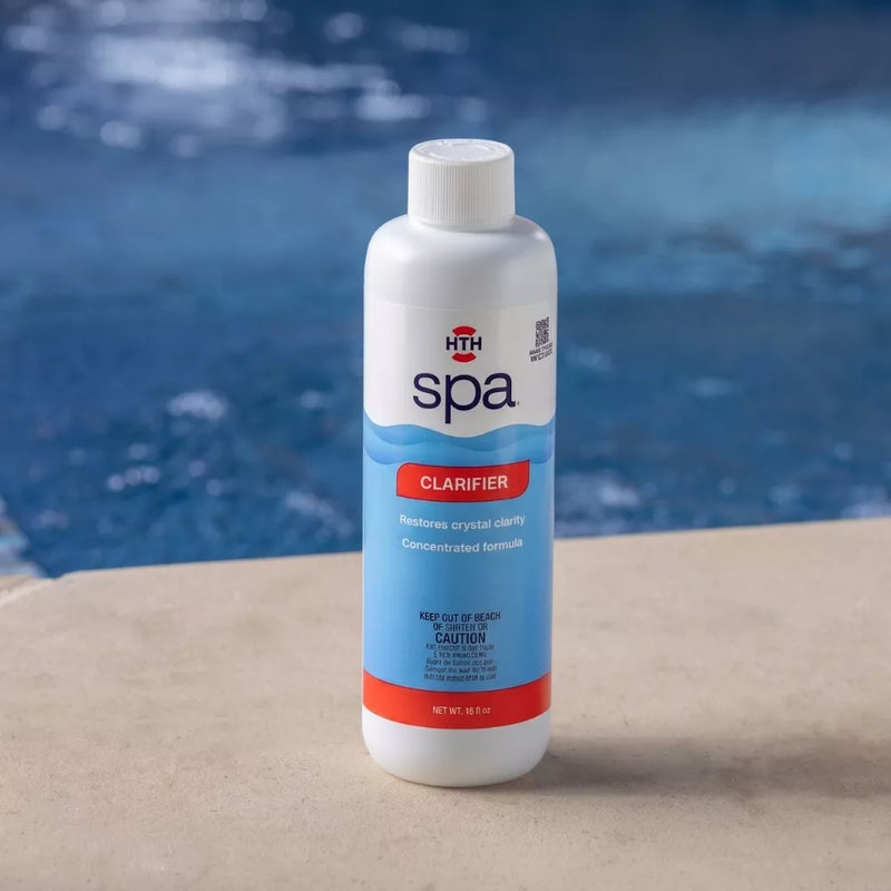 A white bottle of HTH spa concentrated liquid Clarifier sitting on a concrete spa ledge, with the blue water background. The prominent red label highlights 'CLARIFIER' and 'Restores crystal clarity' for spa water. The QR code is also visible.